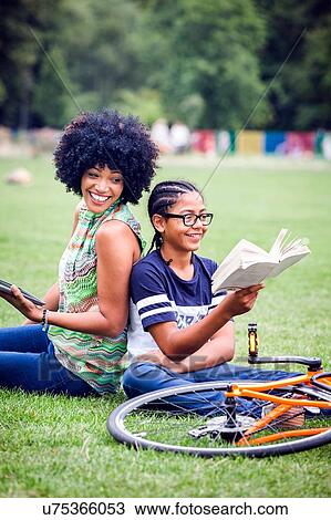 Stock Image - Boy and mother back to back in park reading book. Fotosearch