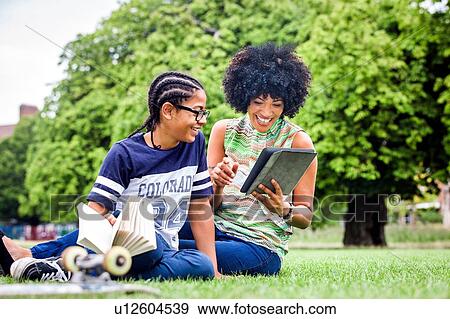 Stock Photo - Boy and mother reading digital tablet in park. Fotosearch