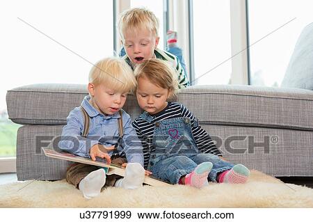 Boy and two toddlers reading childrens book on living room floor View Large Photo Image Stock Photo - Boy and two toddlers reading childrens book on living room floor. Fotosearch