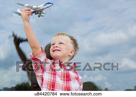 Picture - Boy holding up toy airplane in front of house window. Fotosearch