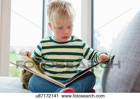 Stock Image - Boy sitting on sofa reading a book. Fotosearch