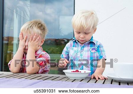Boy with covering eyes whilst toddler brother eats a bowl of raspberries View Large Photo Image Stock Image - Boy with covering eyes whilst toddler brother eats a bowl of raspberries. Fotosearch