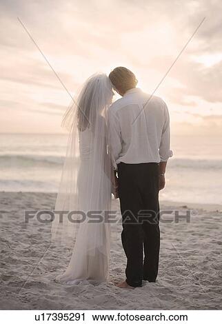 Bride and groom on beach, holding hands, rear view View Large Photo Image Stock Image - Bride and groom on beach, holding hands, rear view. Fotosearch