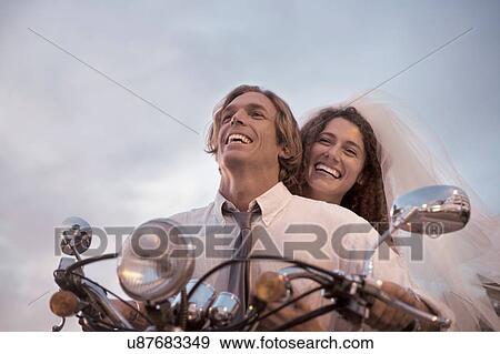 Stock Photo - Bride and groom riding motorcycle against sunset. Fotosearch