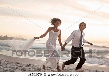 Bride and groom running on beach against sunset View Large Photo Image Stock Image - Bride and groom running on beach against sunset. Fotosearch
