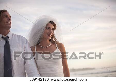 Stock Image - Bride and groom walking along beach. Fotosearch