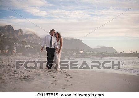 Bride and groom walking along beach View Large Photo Image Stock Photo - Bride and groom walking along beach. Fotosearch