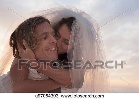 Bride riding piggyback and kissing groom against sunset View Large Photo Image Stock Image - Bride riding piggyback and kissing groom against sunset. Fotosearch