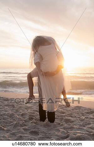 Bride riding piggyback on groom on beach against sunset View Large Photo Image Stock Image - Bride riding piggyback on groom on beach against sunset. Fotosearch