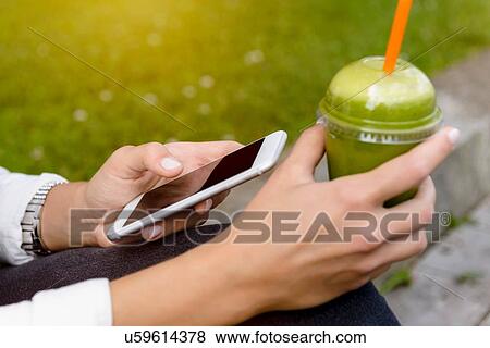 Close up of young woman sitting with smootie drink using smartphone View Large Photo Image Stock Photo - Close up of young woman sitting with smootie drink using smartphone. Fotosearch