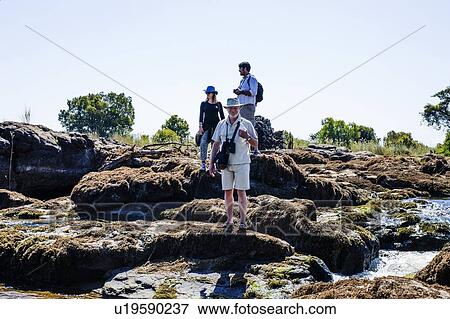 Stock Photo - Couple and mature man on rocks, near Victoria Falls, Zambia. Fotosearch