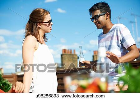 Couple chatting and drinking beer at rooftop party View Large Photo Image Stock Image - Couple chatting and drinking beer at rooftop party. Fotosearch