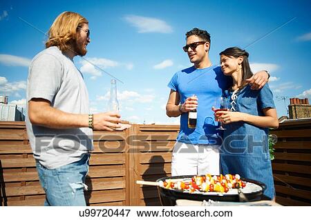 Couple chatting to male friend at rooftop party View Large Photo Image Stock Photo - Couple chatting to male friend at rooftop party. Fotosearch