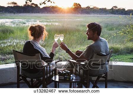 Stock Photo - Couple making wine toast at sunset at safari lodge, Kafue National Park, Zambia. Fotosearch
