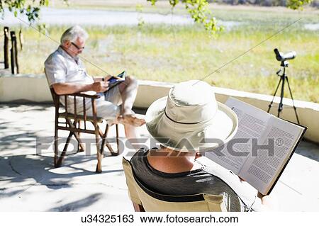 Stock Image - Couple reading books at safari lodge, Kafue National Park, Zambia. Fotosearch