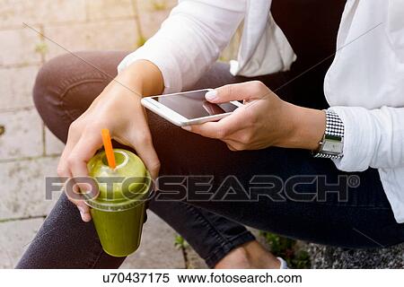Cropped shot of young woman sitting with smootie drink using smartphone View Large Photo Image Stock Photography - Cropped shot of young woman sitting with smootie drink using smartphone. Fotosearch