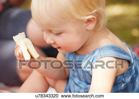 Stock Image - Cropped view of baby girl holding sandwich looking down. Fotosearch