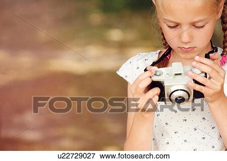 Cropped view of girl holding film camera looking down View Large Photo Image Stock Photo - Cropped view of girl holding film camera looking down. Fotosearch