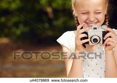 Stock Photo - Cropped view of girl holding film camera eyes closed smiling. Fotosearch