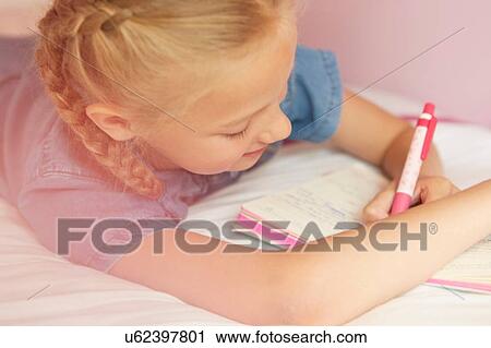 Stock Image - Cropped view of girl on bed writing in notebook. Fotosearch