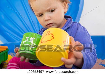 Curious female toddler playing with cups in garden View Large Photo Image Stock Photo - Curious female toddler playing with cups in garden. Fotosearch
