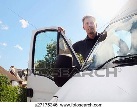 Stock Photograph - Delivery man looking out from white van on suburban street. Fotosearch