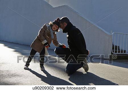 Stock Image - Father and daughter wearing duffle coat head to head in street. Fotosearch