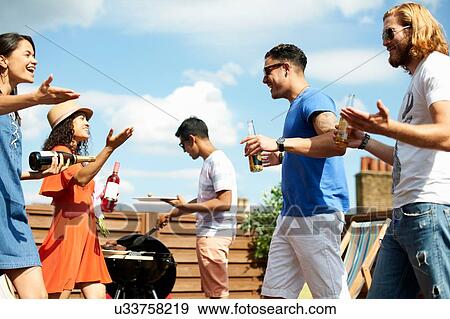 Stock Photo - Female and male friends greeting at rooftop barbecue. Fotosearch