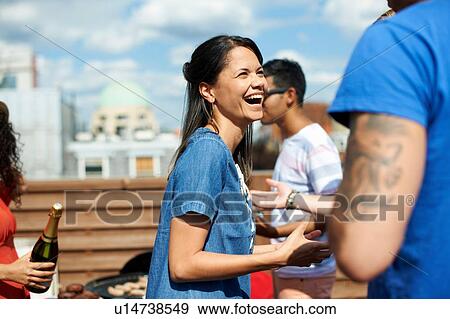 Stock Photo - Female and male friends laughing and chatting at rooftop barbecue. Fotosearch
