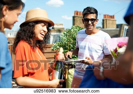 Stock Image - Female and male friends with champagne bottle at rooftop barbecue. Fotosearch