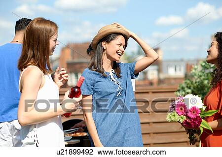 Stock Image - Female friends chatting and laughing at rooftop party. Fotosearch
