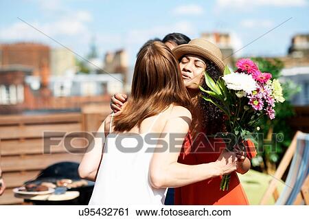 Female friends greeting with flower bouquet at rooftop barbecue View Large Photo Image Stock Image - Female friends greeting with flower bouquet at rooftop barbecue. Fotosearch