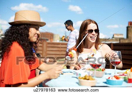 Stock Image - Female friends preparing skewers at rooftop barbecue. Fotosearch
