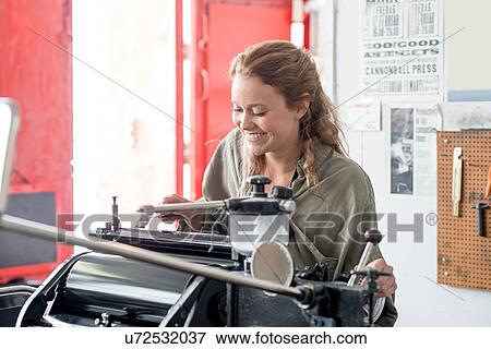 Stock Photo - Female letterpress printer preparing printing machine in workshop. Fotosearch