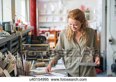Stock Photography - Female print designer examining designs in workshop. Fotosearch