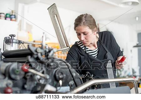 Stock Image - Female printer preparing print machine in workshop. Fotosearch
