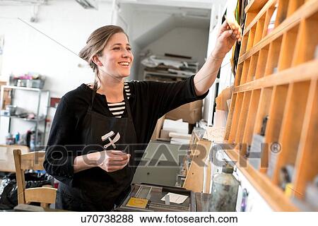 Stock Photo - Female printer selecting letterpress letters from workshop shelf. Fotosearch
