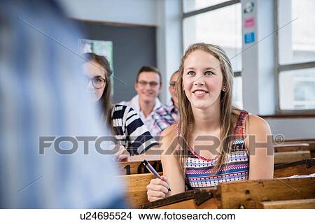 Picture - Female student listening to teacher in classroom. Fotosearch