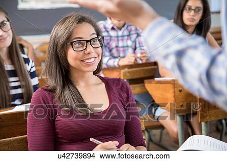 Picture - Female student listening to teacher in classroom. Fotosearch