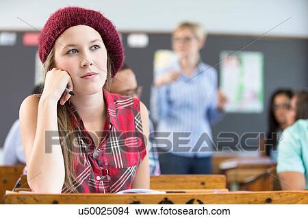 Picture - Female student, sitting at desk in classroom, thinking. Fotosearch