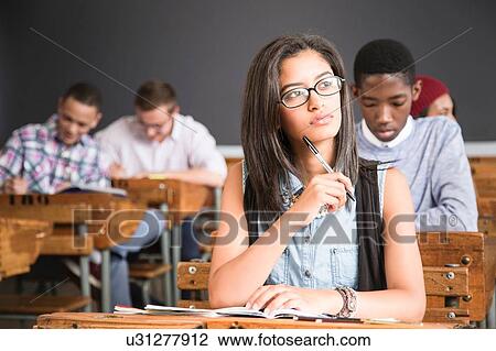 Stock Image - Female student, sitting at desk in classroom, thinking. Fotosearch
