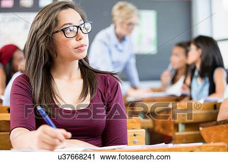 Stock Image - Female student, sitting at desk in classroom, writing. Fotosearch