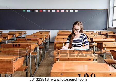 Stock Image - Female student working in empty classroom. Fotosearch