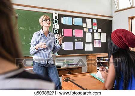 Stock Image - Female teacher addressing students in classroom. Fotosearch