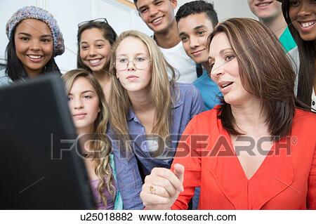 Stock Image - Female teacher explaining on computer to high school students. Fotosearch