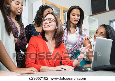 Stock Image - Female teacher explaining on laptop to high school students. Fotosearch