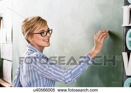 Stock Photography - Female teacher in classroom, writing on blackboard. Fotosearch