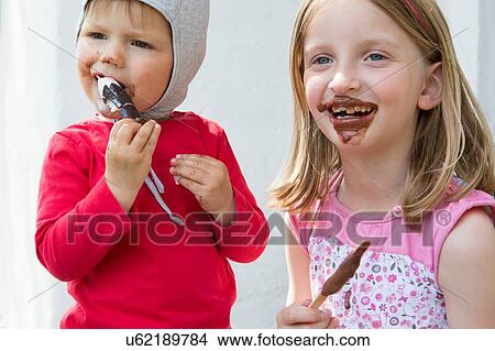 Female toddler and sister messily eating chocolate ice creams View Large Photo Image Picture - Female toddler and sister messily eating chocolate ice creams. Fotosearch
