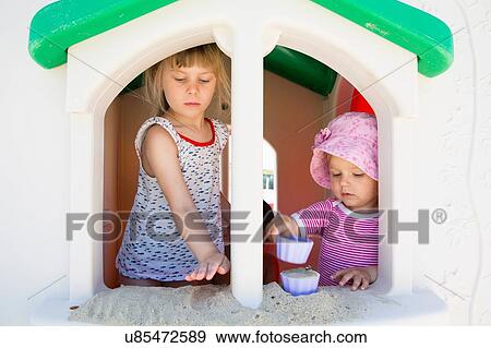 Stock Photo - Female toddler and sister playing with sand on playhouse windowsill. Fotosearch