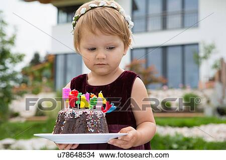 Picture - Female toddler carrying birthday cake with candles in garden. Fotosearch